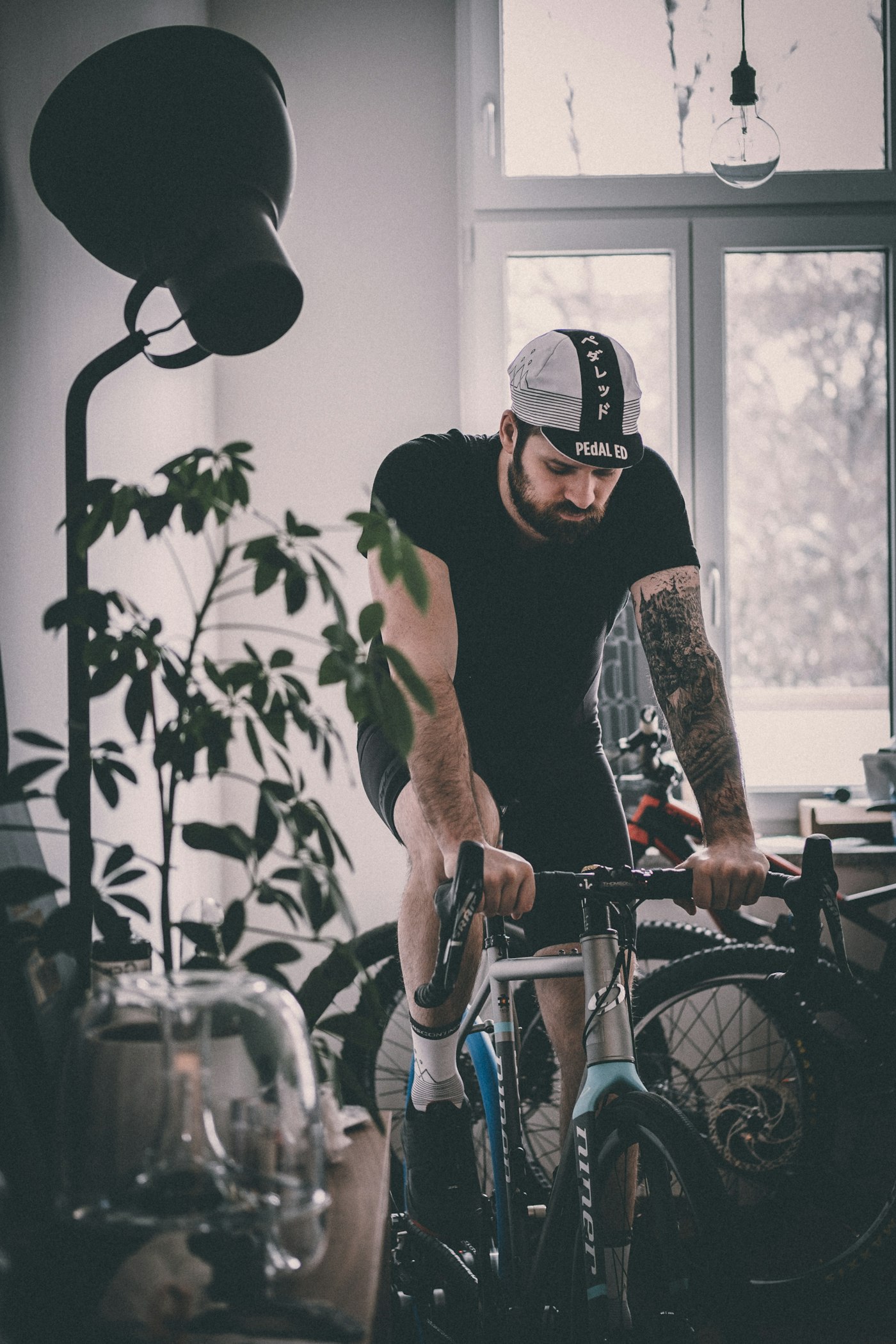 A rider on a road bike mounted on a smart trainer, indoors by a window